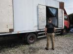 Funkcjonariusz KAS stoi przed otwartymi drzwiami ciężarówki zawierającej linię technologiczną do nielegalnego oczyszczania spirytusu.