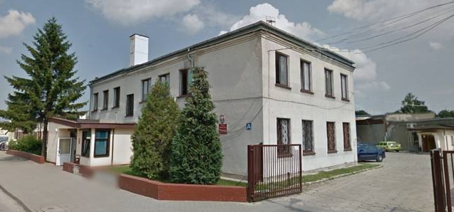 Budynek Urzędu Skarbowego w Aleksandrowie Kujawskim. Zielone krzewy koło budynku i otwarta brama.