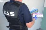 Funkcjonariusz KAS w kamizelce z napisem na plecach trzyma nielegalne papierosy