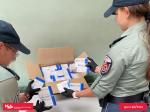 Dwóch funkcjonariuszy  kobieta i mężczyzna stoją tyłem przy stoliku na którym jest karton z opakowaniami leków, które pokazują. 