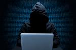 Grafika na tle ściany z cyframi w ciemnym stroju siedzi przed laptopem człowiek w bluzie z kapturem na twarzy, której nie widać.