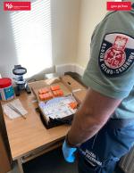 Funkcjonariusz KPUCS stoi przed biurkiem na którym leżą opakowania zatrzymanych środków sterydów i hormonów.