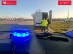 Zdjęcie z wnętrza radiowozu SCS widać sygnał świetlny niebieski, na zewnątrz samochodu stoi funkcjonariusz SCS z zatrzymanym do kontroli kierowcą przy samochodzie dostawczym.