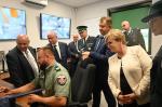 Grupa osób stoi w pomieszczeniu rozmawiają z funkcjonariuszem siedzącym przy biurku.
