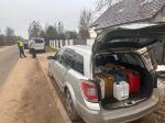 Na 1 planie samochód z zaklejoną boczną szybą. W otwartym bagażniku kilka kanistrów do paliwa. W tle funkcjonariusz i zatrzymany mężczyzna.
