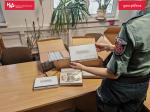 Funkcjonariusz SCS trzyma w dłoni opakowanie z zatrzymanym towarem podczas kontroli, na biurku leżą otwarte kartony z zatrzymanymi towarami.