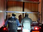 Funkcjonariusz SCS i Policji stoją za otwartą naczepą, wewnątrz widać kartony.