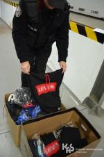 Funkcjonariusz KAS trzymający w ręku podrobioną odzież. Na podłodze stoi karton z podrobionymi towarami.