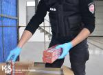 Funkcjonariusz w rękawiczkach wyjmuje z kartonu paczki z nielegalnymi papierosami