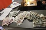 Na stole rozłożone są banknoty, leżą klucze, ruter wifi